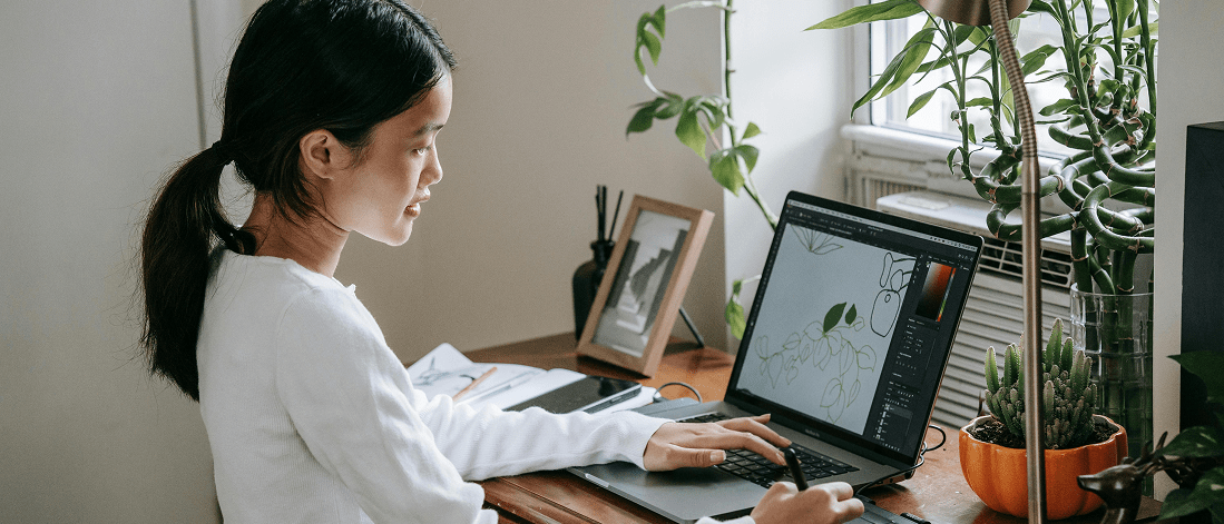 Woman sketching a leaf on a digital tablet at her desk, blending creativity and AI in brand identity design