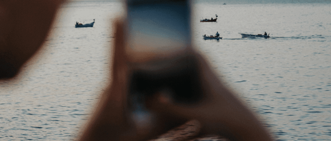 Blurry smartphone capturing fishing boats at sea during golden hour, symbolizing spontaneous user generated content (UGC) in real life.