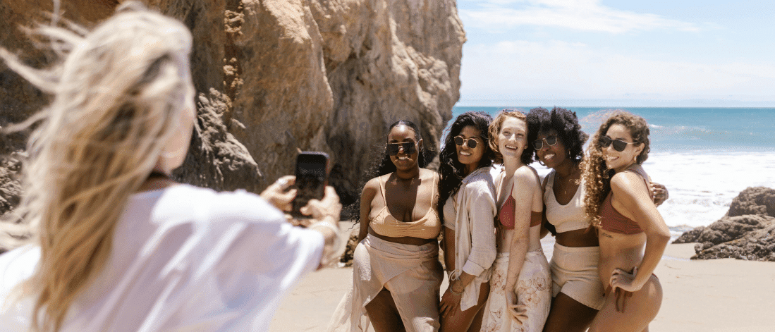Group of diverse women posing for a beach photo taken on a smartphone, representing authentic user generated content (UGC) shared in real moments.