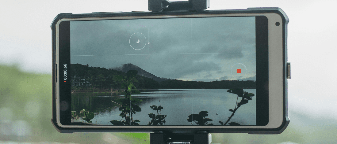 Smartphone recording a peaceful lake view with mountains in the background, capturing user generated travel content.