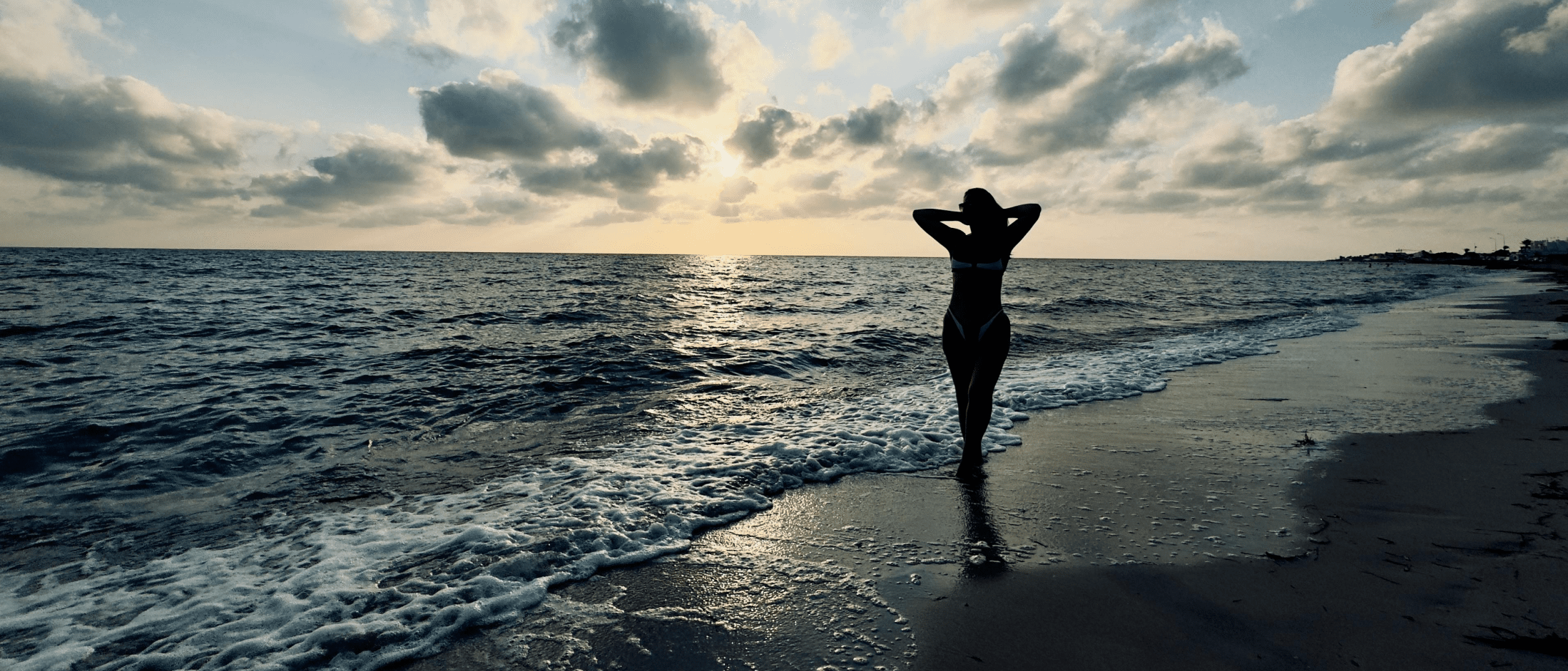 Silhouette of a woman walking along the shore at sunset, symbolizing resilience and personal transformation.