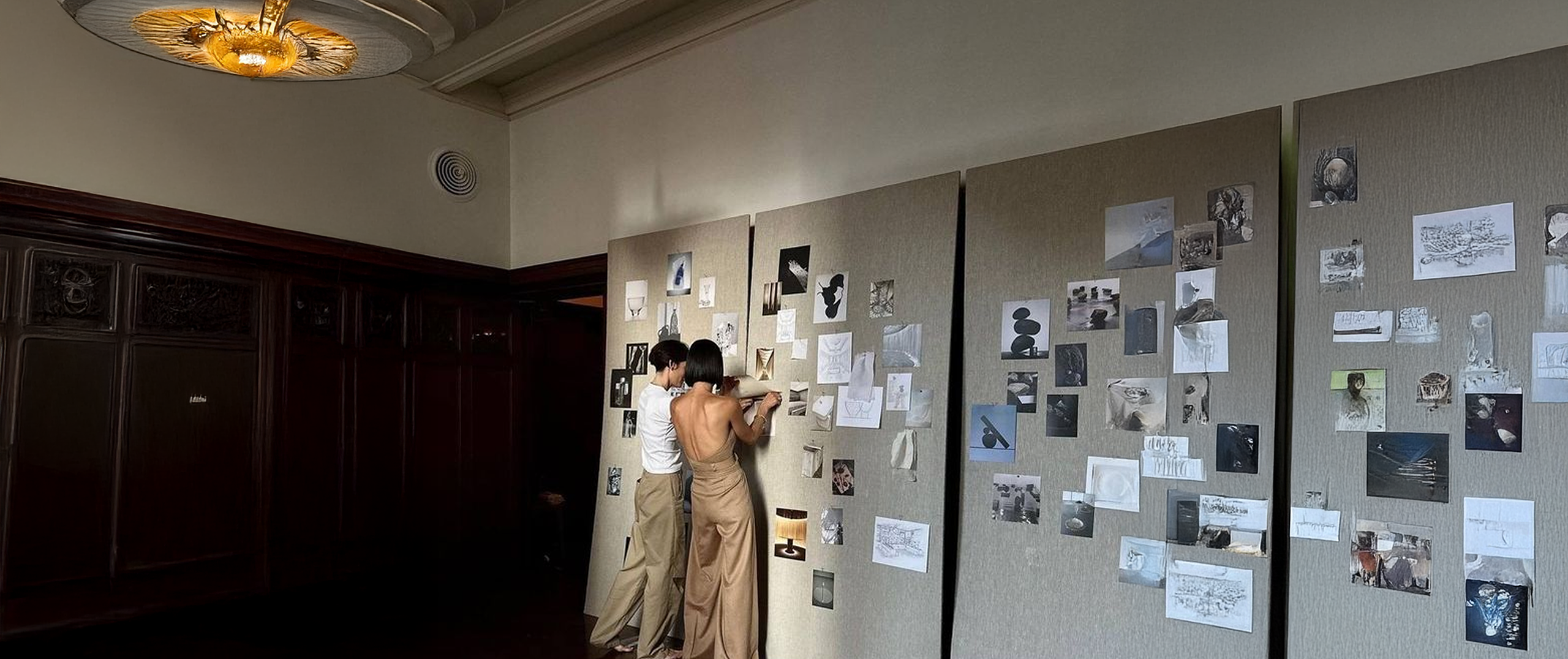 Two people collaborating on a wall of visuals and notes, representing community engagement and shared contribution.