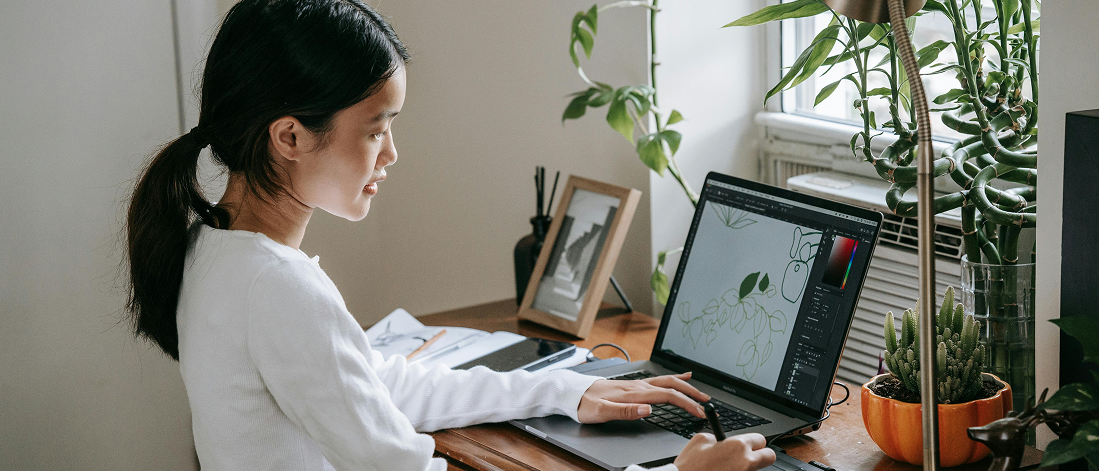 Woman sketching a leaf on a digital tablet at her desk, blending creativity and AI in brand identity design