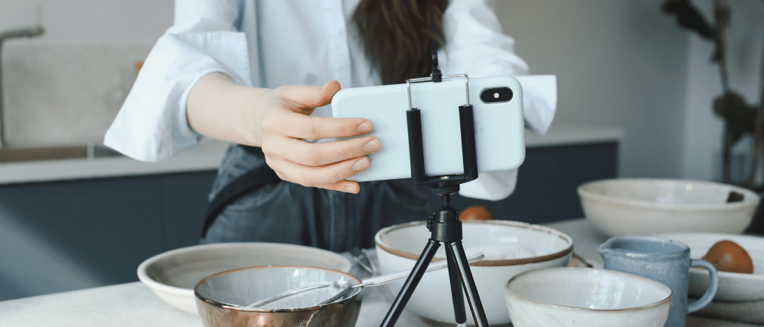 Woman setting up a smartphone on a tripod to film a cooking video, representing user generated content (UGC) creation in a kitchen setting.