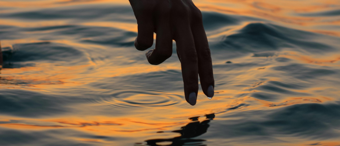 Hand gently touching the water at sunset, symbolizing calm, reflection, and personal growth.