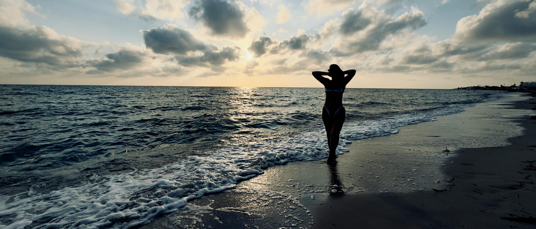 Silhouette of a woman walking along the shore at sunset, symbolizing resilience and personal transformation.